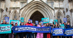 Climate justice protesters are holding banners and posters in front of the Royal Courts of Justice in London. The three claimants, Kairin van Sweeden, Jeremy Cox and Mikaela Loach, who took the government to court over public money being given to oil and gas companies, are front and centre holding a blue banner that says “Paid to Pollute: The case against public money for oil and gas”.