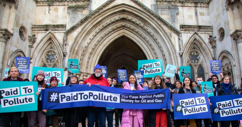 Climate justice protesters are holding banners and posters in front of the Royal Courts of Justice in London. The three claimants, Kairin van Sweeden, Jeremy Cox and Mikaela Loach, who took the government to court over public money being given to oil and gas companies, are front and centre holding a blue banner that says “Paid to Pollute: The case against public money for oil and gas”.